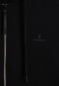 Sudadera con cremallera negra, hecha de tejido texturizado. Presenta una cremallera de metal y un logotipo sutil en la parte frontal. Incluye cordones ajustables.