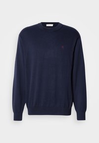 Pull bleu marine à manches longues col rond avec poignets et ourlet côtelés, avec un petit logo rouge brodé sur la poitrine gauche.