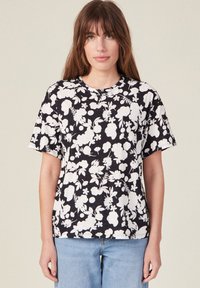 Camiseta negra de algodón con un patrón floral blanco. Presenta mangas cortas y un escote redondo, con un corte relajado y una textura suave.