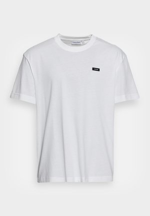 Weißes T-Shirt mit kurzen Ärmeln und Rundhalsausschnitt mit kleinem schwarzem Calvin Klein Logo-Patch auf der linken Brust.