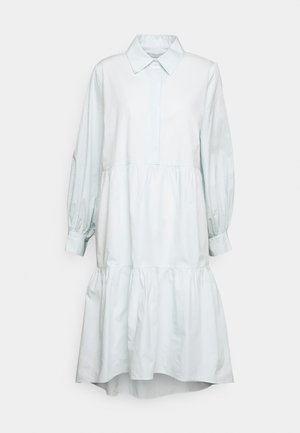 Vaaleansininen paitamekko, joka on valmistettu sileästä kankaasta. Siinä on kaulus, pitkät puffihihat ja kerroksellinen helma, jossa takapää on hieman pidempi.