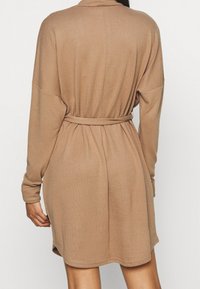 Robe beige à manches longues avec une ceinture, présentant une texture douce, une coupe décontractée et des détails de couture subtils. Arrive au-dessus des genoux.