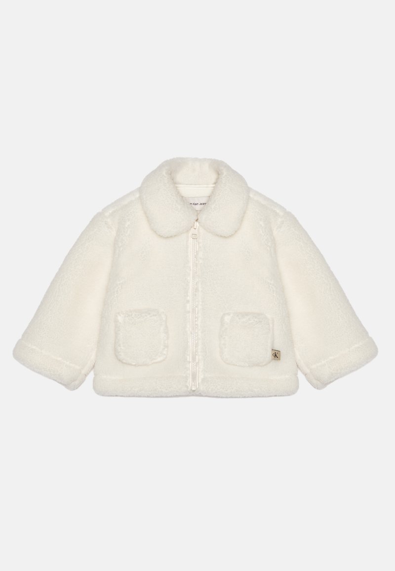 Valge, fliisist jakk koos krae, esipaneeli tõmbluku ja kahe kleebitava taskuga. Omab pehmet tekstuuri ja veidi üle mõõdu suurust.