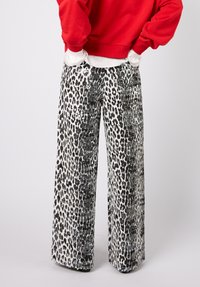 Leveälahkeiset housut mustavalkoisella leopardikuviolla, joissa on teksturoitu, paljetein koristeltu pinta. Yhdistetty punaisella hupparilla vyötäröllä.