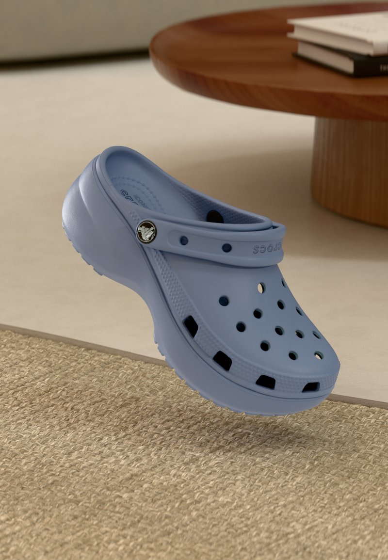 Lichtblauwe Crocs klompen van degelijk plastic, voorzien van ventilatiegaten, een draaibare band en een getextureerde zool.