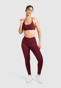 Bordeaux sportbeha en hooggetailleerde leggings gemaakt van een soepele, rekbare stof. Witte sportschoenen met subtiele branding maken de outfit compleet.