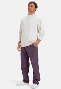 Svetle šedá mikina s dlouhými rukávy a kulatým výstřihem, kombinovaná s volnými hluboce fialovými kordovými kalhotami a bílými teniskami.