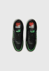 Zwarte sneakers van mesh en leer, met groene accenten op de randen en een rode hartlogo op de binnenzolen, voorzien van zwarte veters en tong.