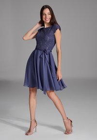 Robe bleu marine avec corsage en dentelle, manches courtes et jupe évasée fluide. Présente une ceinture en tissu à la taille et une texture lisse en chiffon.