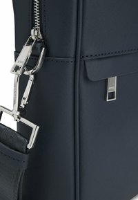 Granatowa skórzana torba na laptopa o fakturowanym wykończeniu, srebrne okucia, zapięcie na suwak oraz odpinany pasek na ramię. Subtelne detale z logo.
