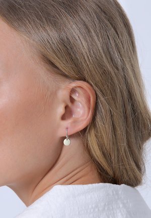 Pendientes de aro de plata con un pequeño colgante en forma de disco circular. El diseño es minimalista y el acabado parece pulido y reflectante.