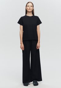 Czarny, krótki rękaw t-shirt połączony z szerokimi czarnymi spodniami, oba wykonane z gładkiego materiału. Charakteryzuje się prostym, minimalistycznym wzornictwem.