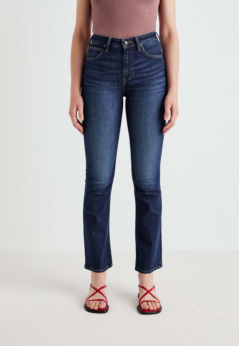 Hoge taille, donkerblauwe jeans met een rechte pijp, voorzien van voorzakken en een subtiele vervaging. Gestyled met rode sandalen met bandjes.