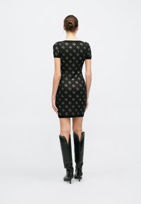 Μαύρο εφαρμοστό φόρεμα με κοντά μανίκια και περίπλοκο χρυσό μοτίβο σε σχήμα ρόμβου. Συνδυάζεται με μαύρες μπότες μέχρι το γόνατο με μυτερή άνω πλευρά.