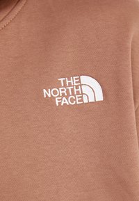 Sudadera de cuello redondo marrón hecha de un tejido suave, con un logotipo bordado en blanco en el lado izquierdo del pecho con un diseño curvo.