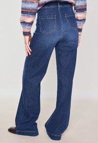 Jeans a zampa d'elefante in denim blu scuro, con vita alta, due tasche posteriori e una silhouette a gamba dritta con un orlo curato.