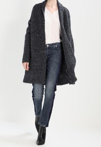 Ciemnoszary, teksturowany wełniany płaszcz z szalem, noszony na jasnej bluzce i niebieskich dżinsach. Czarne botki na obcasie dopełniają zestaw.