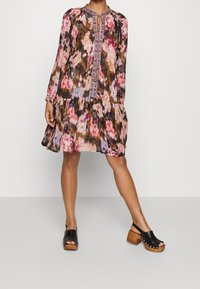 Kukkamekko, jossa on röyhelöhame, pitkät hihat ja kirjailtu pääntie. Värit sisältävät vaaleanpunaisen, ruskean ja violetin. Yhdistetty mustiin korkokenkiin.