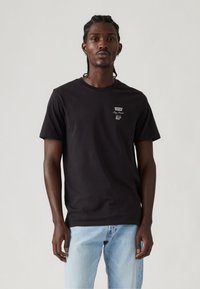 Crna pamučna majica s okruglim izrezom i kratkim rukavima, s malim Levi's logom na prsima. Nosimo je s svijetloplavim trapericama.
