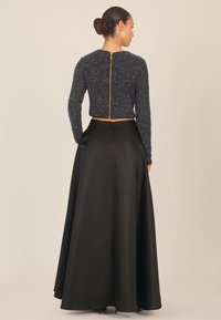 Schwarzer Satin-Bodenlanger Rock, kombiniert mit einem kurz geschnittenen, strukturierten navy-blauen Pullover mit einem goldenen Reißverschluss auf der Rückseite und langen Ärmeln.