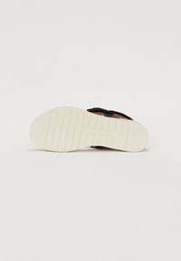 Sandale noire avec sangle réglable, semelle en liège et semelle en caoutchouc blanc et strié. Accentuée par un logo subtil sur la semelle.