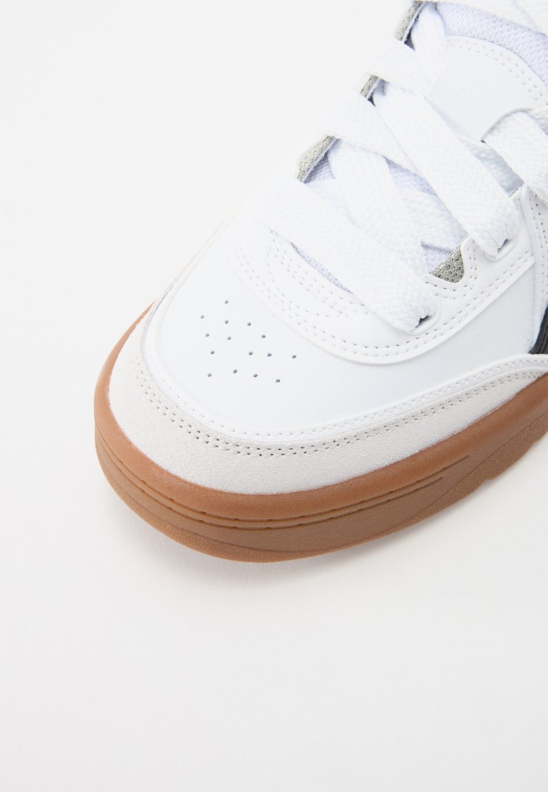 Sneaker bianco con tomaia in pelle, dettagli in suede grigio, punta perforata e suola in gomma marrone. Lacci testurizzati completano il design.