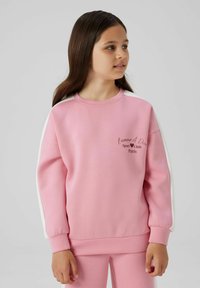 Sudadera rosa con franjas laterales blancas, puños acanalados y un gráfico frontal que dice "L'amour A Deux Sport Club Paris". Tejido suave, corte relajado.