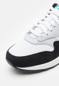 Baskets avec une tige en maille blanche, un accent en suède noir et une surcouche en cuir gris. Design à lacets avec une semelle en caoutchouc noir.