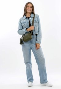 Green leather crossbody bag with zipper closure, leather tassel accents, rectangular shape, and adjustable strap, displayed with denim outfit.