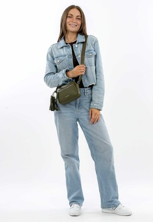 Green leather crossbody bag with zipper closure, leather tassel accents, rectangular shape, and adjustable strap, displayed with denim outfit.