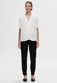 Biela blúzka s krátkymi rukávmi a V-št neckline s jemnou textúrou, kombinovaná s čiernymi slim-fit nohavicami a plochými čiernymi topánkami. Jednoduchý, elegantný dizajn.