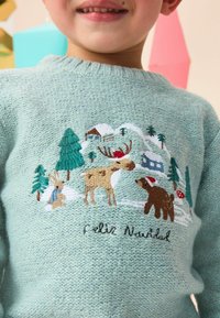 Pull en maille bleu clair avec une broderie festive d'un lapin, d'un renne, d'un ours, d'arbres et d'une maison avec le texte "Felix Navidad".