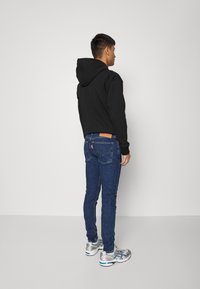 Sweatshirt preto com capuz, jeans skinny azul escuro com detalhe nos bolsos de trás, e sapatilhas cinzas. Design simples, ajuste casual e textura suave.