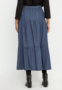 Jeansmaxikjol med ett samlat, flerradigt mönster, mörkblå färg, elastisk midja och en svävande silhuett. Kombinerad med svarta ankelskor.