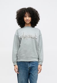 Pelēks džemperis ar apaļu kaklu, rotāts ar mirdzošu uzrakstu "respect" no rhinestones. Kombinēts ar ikdienišķiem zilajiem džinsiem.