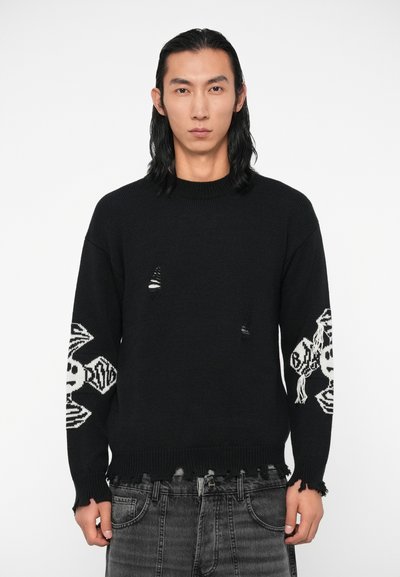 Maglione nero lavorato a maglia con strappi visibili, caratterizzato da modelli di teschio e ossa incrociate bianchi sulle maniche, polsini a coste e dettagli di orlo irregolare.