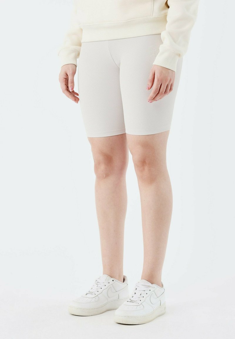 Shorts de vélo à côtes beige clair, en matériau extensible. Portés avec un sweat-shirt crème et des baskets blanches. Longueur mi-cuisse.