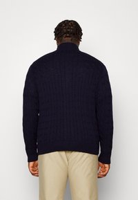 Marinblå kabelstickad tröja med hög krage, ribbade ärmslut och nederkant, med ett strukturerat mönster och en avslappnad passform.