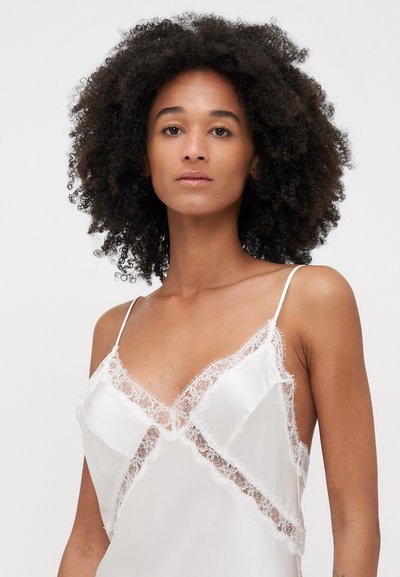 Weißes Satin-Camisole mit Spitzenbesatz, dünnen Trägern und V-Ausschnitt. Die glatte Textur und die zarten Details erzeugen ein schichtartiges Erscheinungsbild.