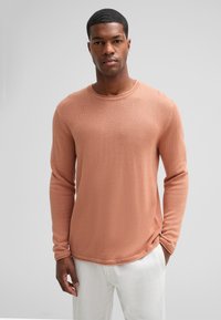 Maglione a maniche lunghe, collo rotondo, di un morbido colore pesca con un motivo a maglia testurizzato, abbinato a pantaloni bianchi. Finitura liscia, design informale.