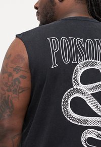 Svart ermeløs skjorte med stor hvit "POISON" tekst og et slangegrafikk på baksiden, laget av et mykt, teksturert stoff.