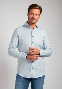 Lichtblauw geruit overhemd met een gestructureerde kraag, groene knopen, lange mouwen en een ronde zoom; gedragen met blauwe jeans.