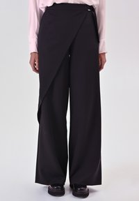 Pantaloni neri a gamba larga con un pannello frontale asimmetrico, realizzati in un tessuto liscio. Presentano un design minimalista e una finitura pulita.