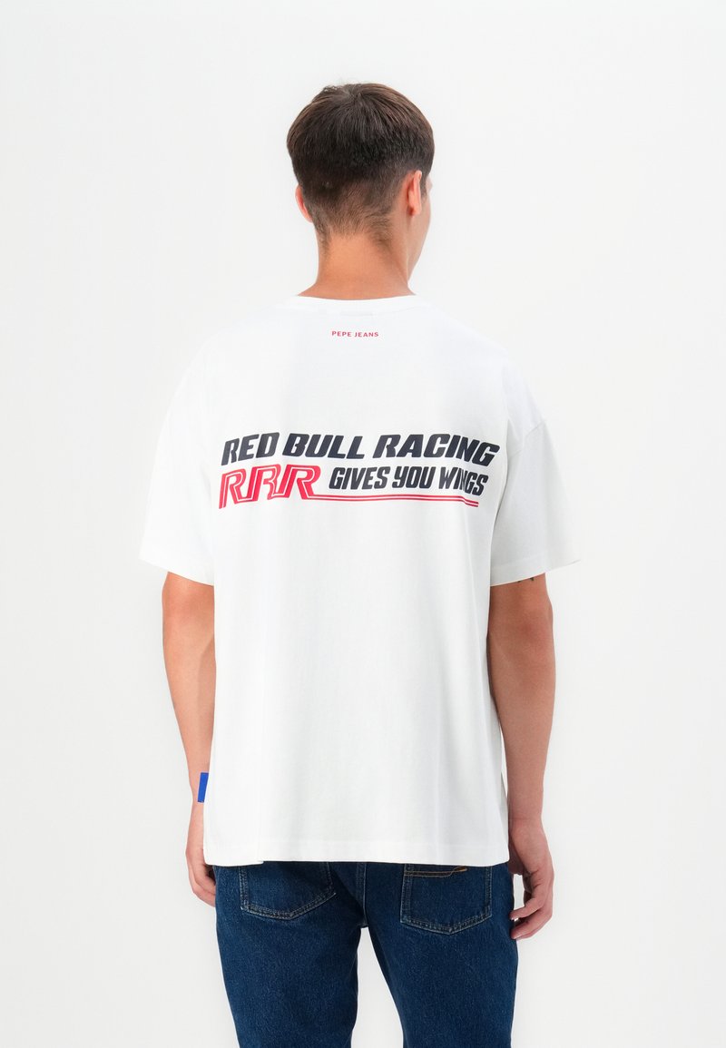 Balta kokvilnas T-kreklā ir liels melns un sarkans grafiskais prints aizmugurē ar uzrakstu "RED BULL RACING RRR GIVES YOU WINGS."