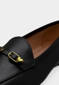 Μαύρο δερμάτινο μοκασίνι με χρυσή αγκράφα σε σχήμα καρδιάς χαραγμένη με τη φράση "LOVE MOSCHINO", που απεικονίζει λεία υφή και ταμπά εσωτερική επένδυση.