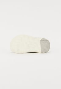 Suela de zapatilla blanca con un patrón texturizado y estriado. La base presenta una forma redondeada y un acabado suave, con sutiles acentos grises cerca del borde.