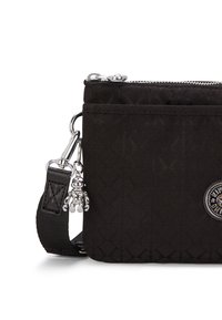 Borsa in tessuto trapuntato nero con zip e componenti in argento. Presenta un charm decorativo e una tracolla rimovibile. Dettaglio del logo circolare visibile.