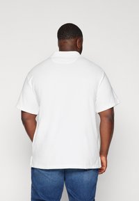 Polo bianca in cotone con colletto e maniche corte, caratterizzata da un taglio dritto e spacchi laterali. Tessuto morbido e dettagli minimali.