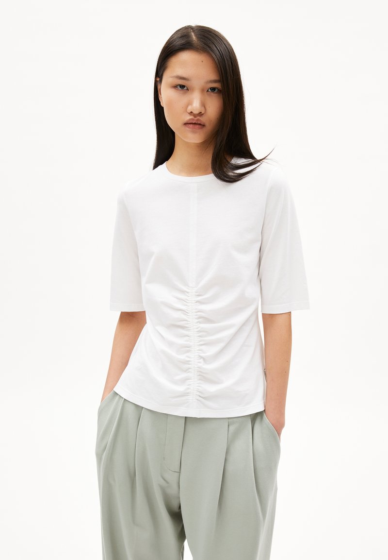 Witte T-shirt met korte mouwen en opgehoopte details in het midden, gemaakt van zachte stof, gecombineerd met lichtgroene geplooide broeken.