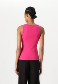Enges, ärmelloses Oberteil in leuchtendem Pink, aus dehnbarem Stoff. Verfügt über einen runden Ausschnitt und eine glatte Verarbeitung. Schwarze Hosen sind darunter sichtbar.